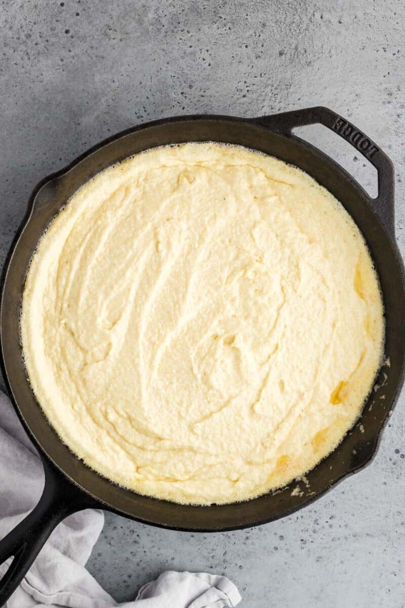 A cast iron skillet filled with a smooth, creamy mixture sits on a gray surface with a cloth partially visible at the bottom.