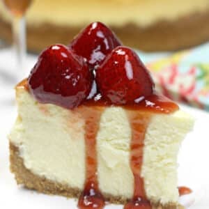 A slice of classic cheesecake topped with glazed strawberries and strawberry sauce on a plate.