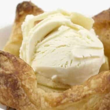 A scoop of vanilla ice cream sits atop a baked pastry with folded corners, served on a white plate.