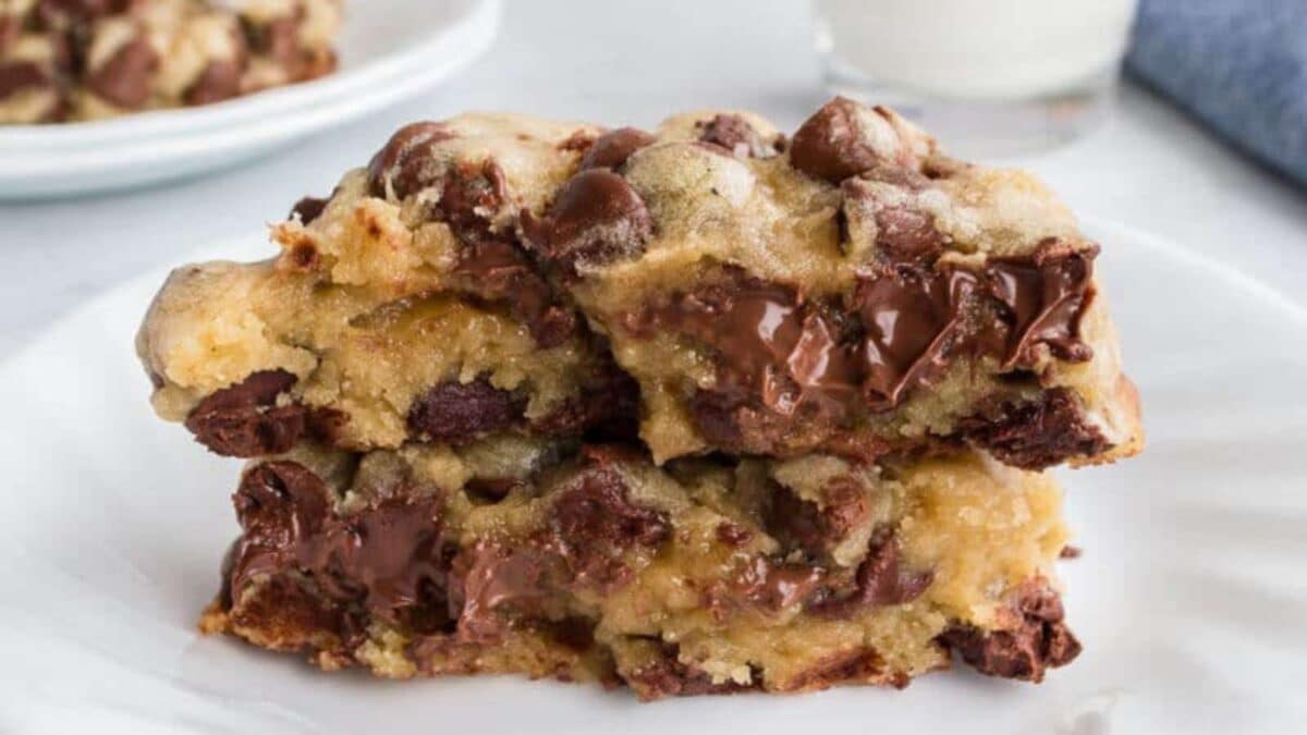 Two thick, gooey chocolate chip cookies stacked on a plate, with melted chocolate pooling visibly.