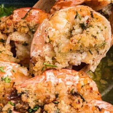 Shrimp topped with a golden breadcrumb crust, garnished with herbs, on a wooden spoon.