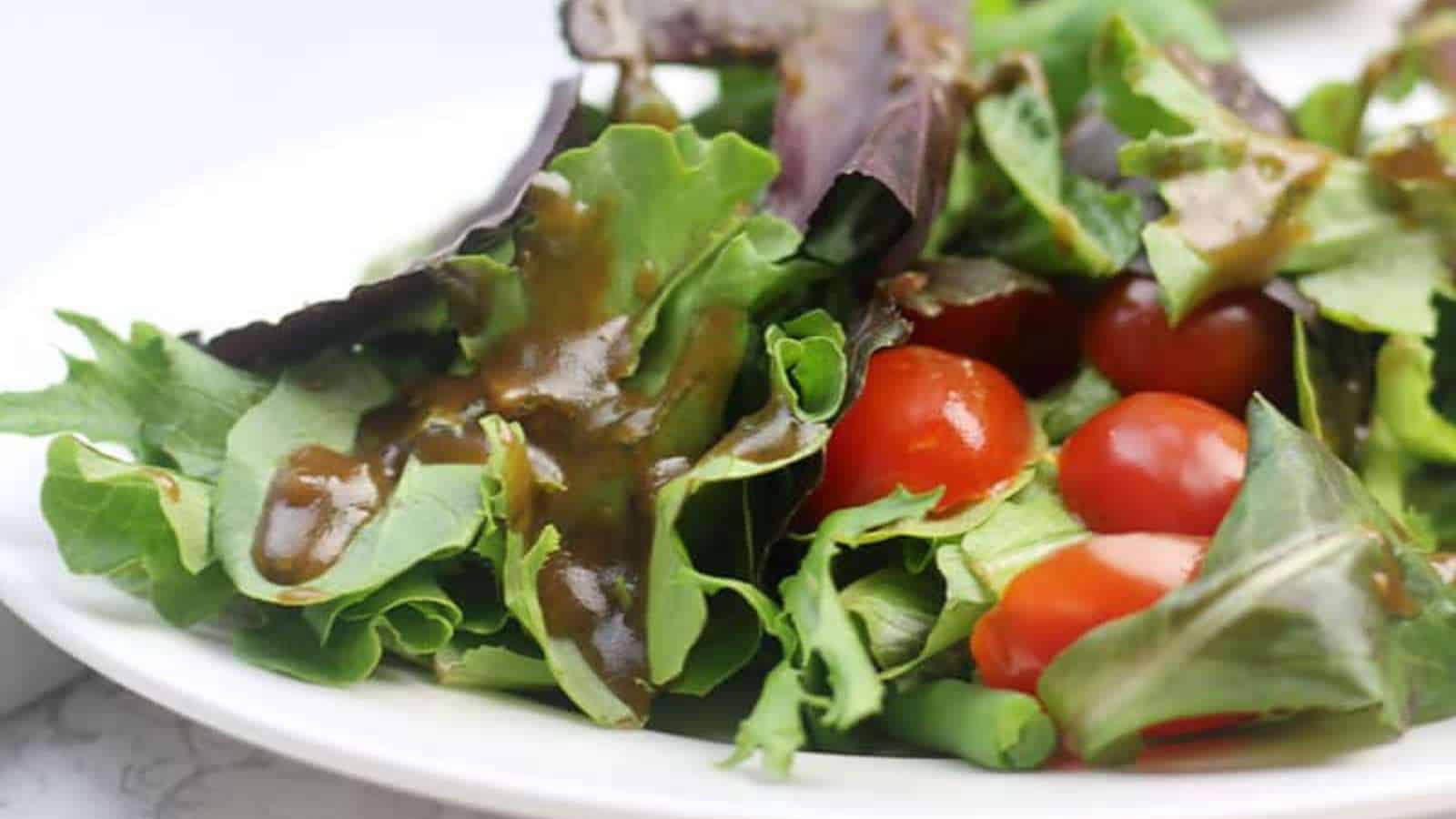 A salad with mixed greens, cherry tomatoes, and brown dressing on a white plate.