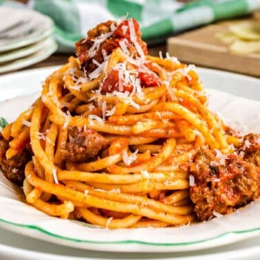 A plate of spaghetti with bolognese sauce, sprinkled with grated cheese, served on a white plate with green trim.