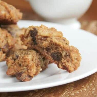 A plate of breakfast cookies, with one cookie broken in half, is placed on a patterned brown cloth.