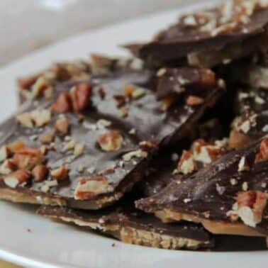 A plate of chocolate-covered butter toffee pieces topped with chopped nuts.