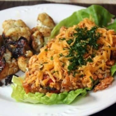 Lettuce wrap filled with chicken and cheese topped with herbs, served with a side of roasted cauliflower on a white plate.