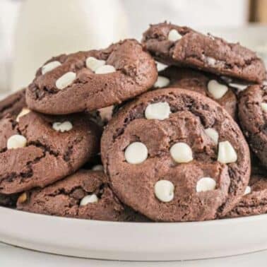 A plate of chocolate cake mix cookies with white chocolate chips stacked on a white plate.