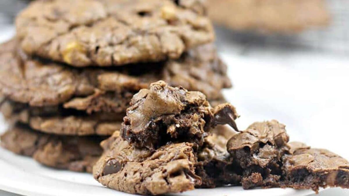 A stack of chocolate peanut butter chip cookies on a plate, with one cookie broken to show the interior.