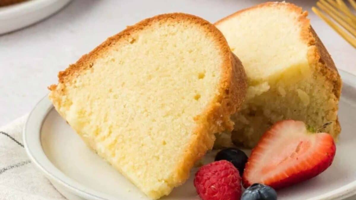 Two slices of pound cake on a white plate, accompanied by strawberries, raspberries, and blueberries.