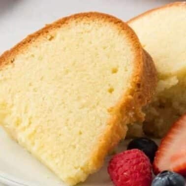 Two slices of pound cake on a white plate, accompanied by strawberries, raspberries, and blueberries.