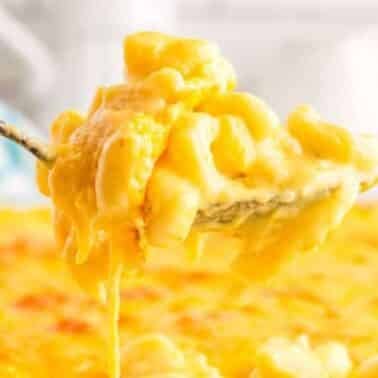 A spoon lifts a serving of creamy macaroni and cheese from a baking dish.