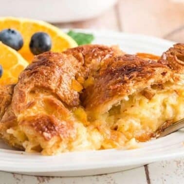 Croissant breakfast casserole on a plate with orange slices and blueberries, accompanied by a fork.