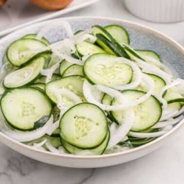 A bowl of cucumber and onion salad on a marble countertop.