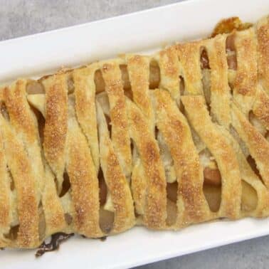 A rectangular lattice apple strudel on a white tray with a golden-brown crust.