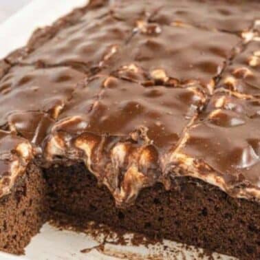 A rectangular Mississippi mud cake in a white dish, with a glossy icing, partially cut into squares. A couple of pieces are missing from one end.