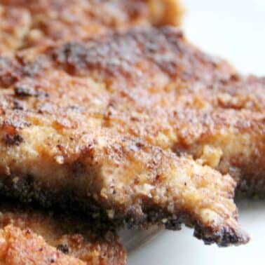 Close-up view of crispy, golden-brown parmesan breaded chicken pieces on a white plate.