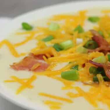 Bowl of creamy potato soup topped with shredded cheese, bacon bits, and chopped green onions.