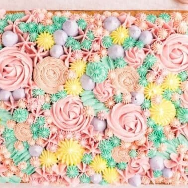 A rectangular cake with intricate pastel floral frosting patterns, including pink roses and various piped designs in blues, yellows, and greens.
