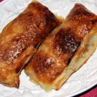 Two golden-brown apple turnovers on a white plate with a textured red background.