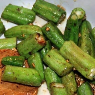 Chopped okra seasoned and sautéed with garlic, shown in a white bowl with a wooden spoon.