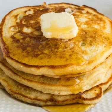 A stack of three pancakes topped with a melting pat of butter and syrup on a white plate.