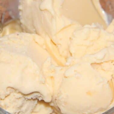 A clear glass bowl filled with several scoops of banana ice cream, with a spoon partially visible on the side.