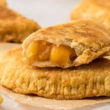 Two baked fried apple hand pies on a parchment, one cut in half showing a filled interior with diced apples.