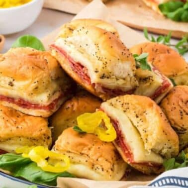 A plate of Italian sliders filled with meat and cheese, topped with seasoning, garnished with yellow pepper slices and herbs.