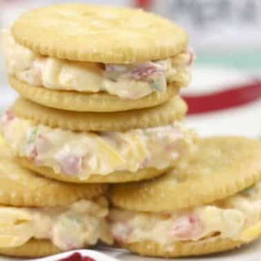 Four cracker sandwiches filled with a creamy jalapeno pimento spread sit on a plate.