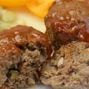 Two glazed meatloaf muffins, one cut open on a white plate.