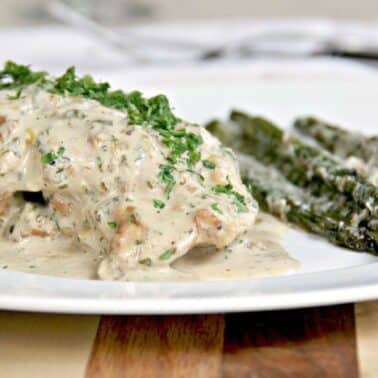 Creamy mustard herb sauce on chicken with a side of roasted asparagus topped with grated cheese on a white plate.