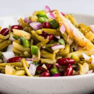 A bowl of three bean salad with red kidney beans, green beans, chopped red onions, green peppers, and wax beans, mixed and seasoned.