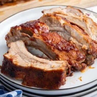Sliced, glazed ribs on a white plate with a blue and white checkered cloth nearby.