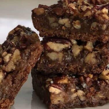 A stack of four pecan pie bars on a plate, featuring a crumbly crust and a nutty top layer.