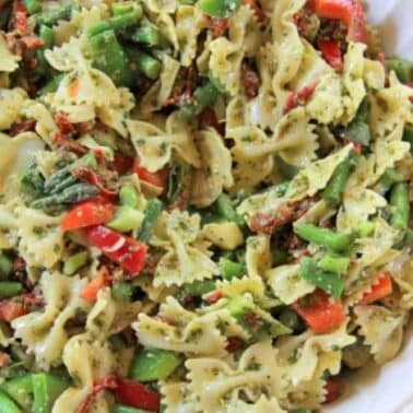 A bowl of bowtie pasta mixed with diced red peppers, green beans, and leafy greens, seasoned with a hint of pesto.