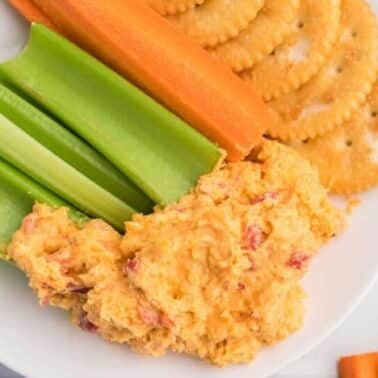Plate with pimento cheese dip, celery sticks, carrot sticks, and round crackers.