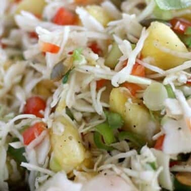 Close-up of a pineapple coleslaw with shredded cabbage, pineapple, bell peppers, and green onions in a blue bowl.
