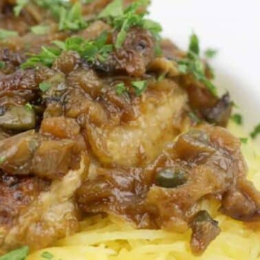 A plate with pork chops topped with sautéed onions and herbs, served on a bed of thin noodles.