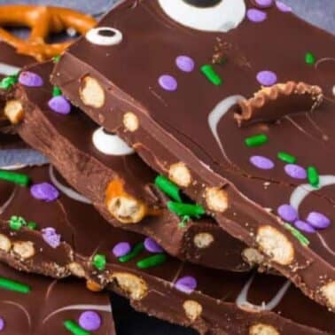 Stack of chocolate bark pieces topped with green and purple sprinkles, pretzels, and candy eyes.