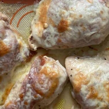 Baked chicken breasts with melted cheese and prosciutto on a silicone baking mat.