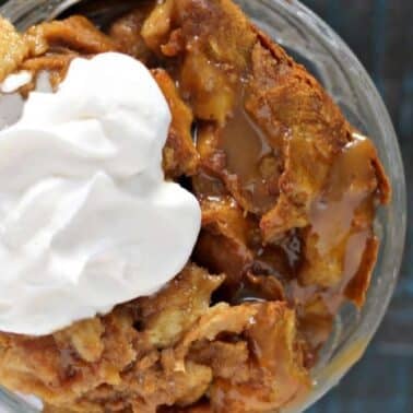 Top view of a dessert with whipped cream on top of caramel-drizzled pumpkin bread pudding in a glass dish.