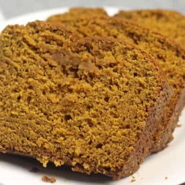 Three slices of pumpkin bread on a white plate, placed on a grey surface.