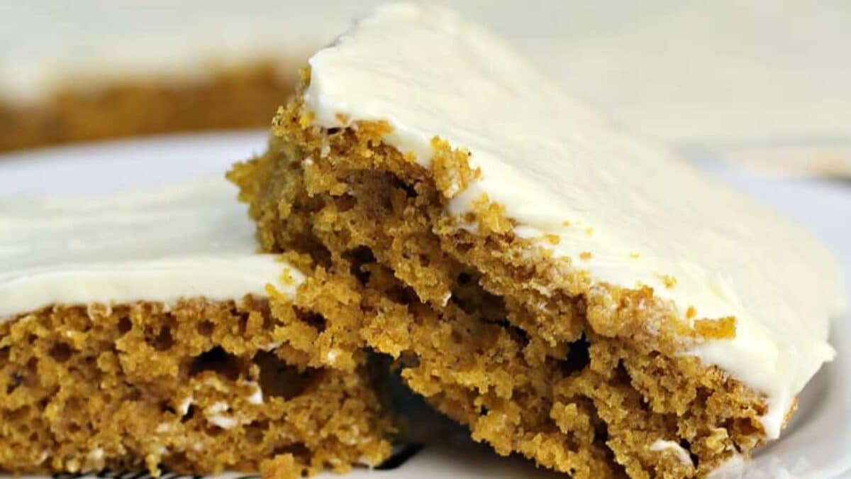 Two slices of frosted pumpkin sheet cake stacked on a plate.