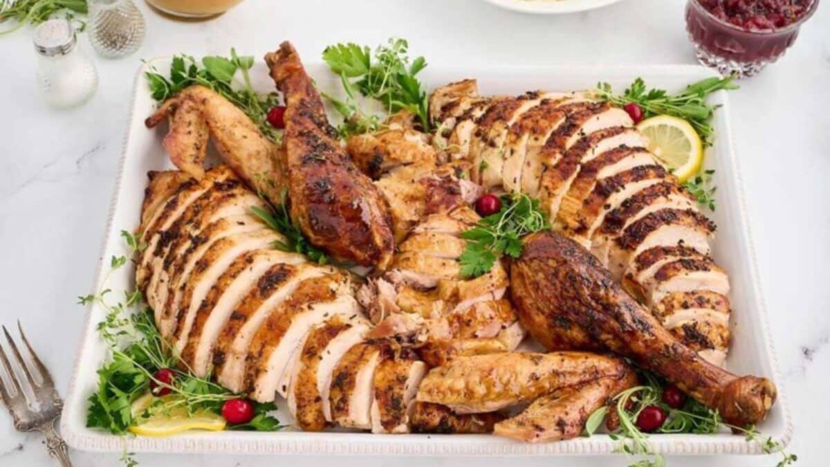 Sliced roasted turkey with herbs, lemon slices, and cranberries on a white platter.