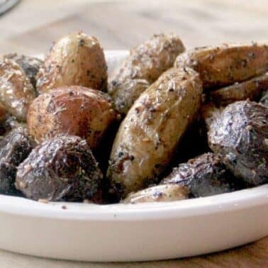A white dish filled with roasted baby potatoes seasoned with herbs, placed on a wooden surface.