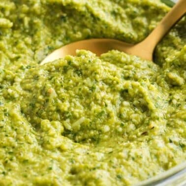A close-up of jalapeno cilantro pesto in a glass bowl with a gold spoon.