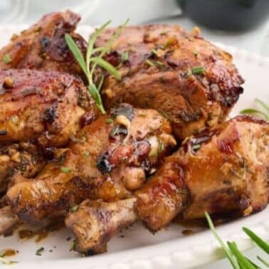Roasted rosemary balsamic chicken pieces garnished with herbs on a white plate.