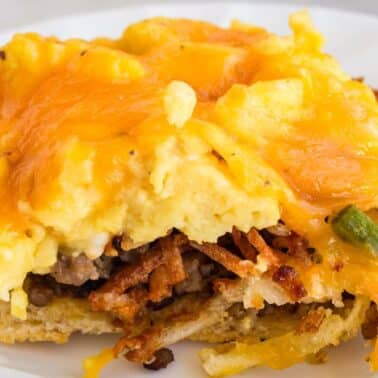 A slice of breakfast pizza with eggs, cheese, hash browns, sausage, and green onions on a white plate.