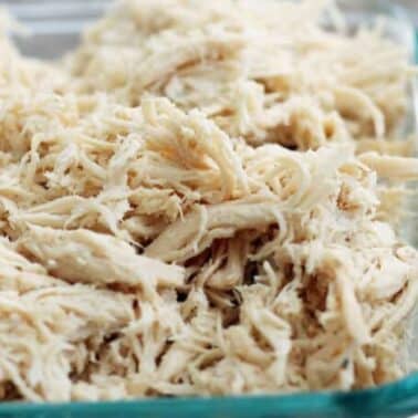 Shredded chicken piled in a clear glass container on a wooden surface.