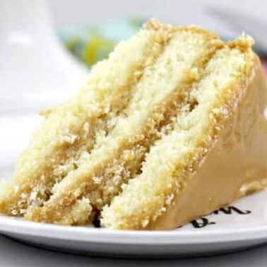 A slice of three-layer cake with caramel frosting, on a white plate.